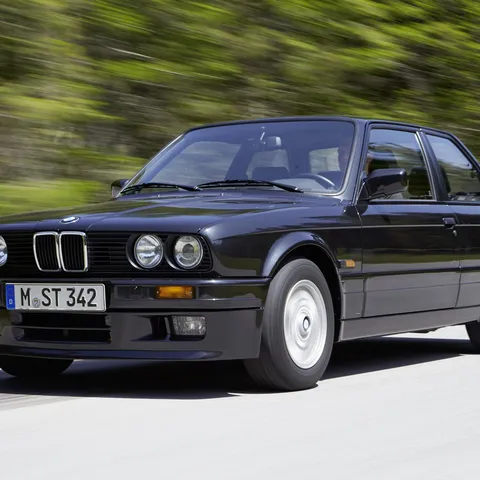 Black BMW E30 320is two-door saloon driving on a mountain road
