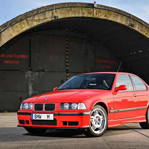 Red BMW E36 M3 Compact prototype parked in front of a bunker