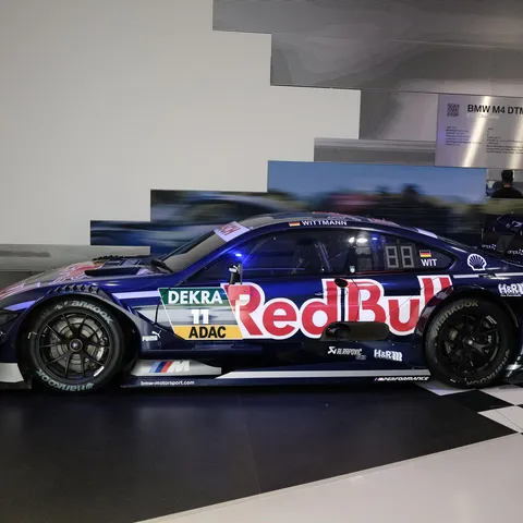 Side view of a dark blue BMW M4 DTM (F82) race car in Red Bull livery on display at the BMW Museum in Munich, featuring a massive rear racing wing, aggressive carbon rear diffuser, Hankook tires, and Marco Wittmann's name on the rear window.